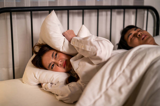 Person covering their ears while a partner snores at night, illustrating allergy related sleep disruption.