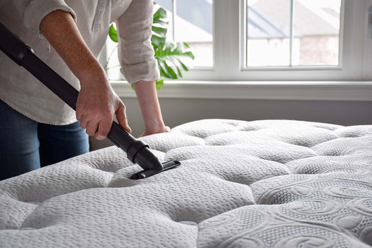 A woman using a vaccum cleaner to reduce allergens in her bedroom