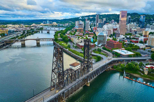 Aerial view of the Portland, Oregon skyline with steel bridges crossing a river, hills and cloudy sky behind
