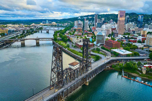 Aerial view of the Portland, Oregon skyline with steel bridges crossing a river, hills and cloudy sky behind