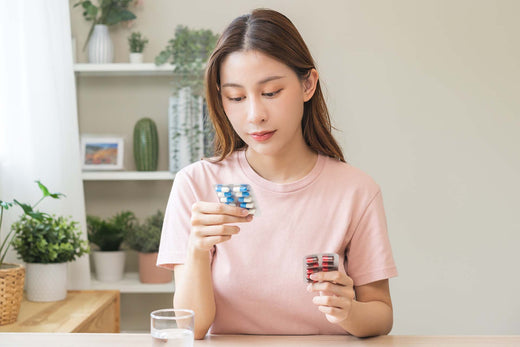 Woman comparing two blister packs of allergy medication capsules with a glass of water at home