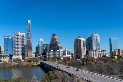 Austin, Texas skyline with high-rise buildings behind a bridge over the river under a clear blue sky