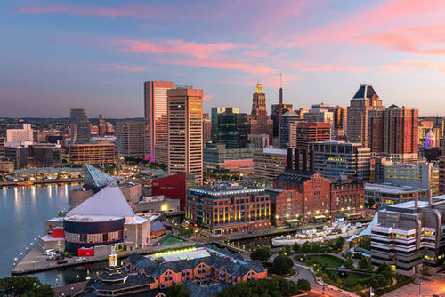 Baltimore, Maryland skyline at dusk over the Inner Harbor, with high-rise buildings and a pink sky