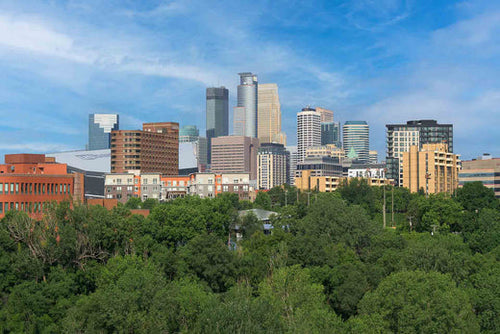 Minneapolis, Minnesota skyline rising above a line of green trees under a blue sky