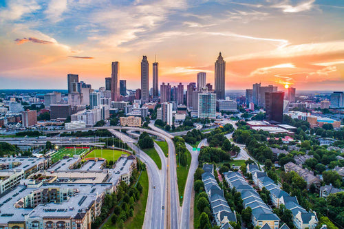 Aerial view of the Atlanta, Georgia skyline at sunset, with highways, buildings, and green trees below