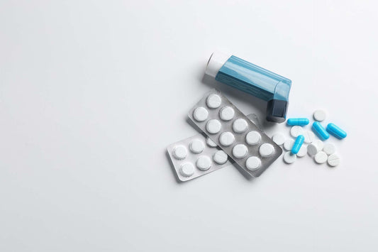Blue inhaler beside blister packs of white tablets and scattered blue and white pills on a light surface