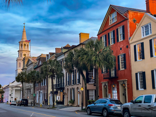 Colorful historic row houses and a church steeple in Charleston, South Carolina, with palm trees at dusk