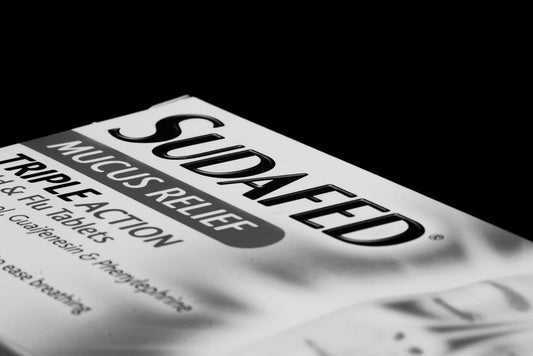 Black-and-white close-up of a box of Sudafed Mucus Relief Triple Action tablets, a decongestant.