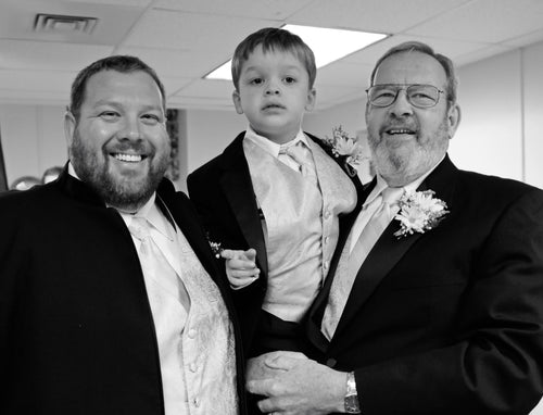 Three generations of a family — a man, a young boy, and an older man — smiling together at a formal event in this black-and-white photo.