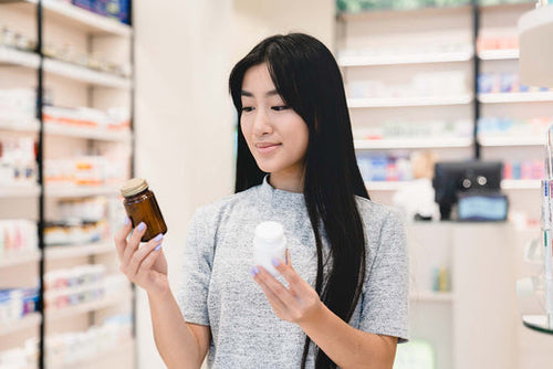 Person in a pharmacy comparing two medication bottles, one in each hand.